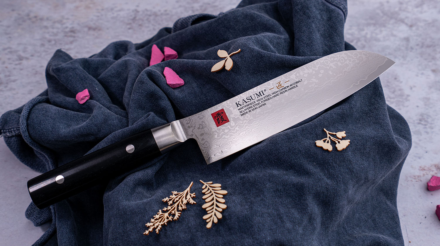 Japoński nóż Santoku Kasumi na granatowej tkaninie z ozdobnymi elementami.