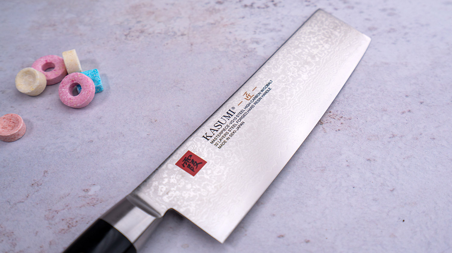 Japoński nóż Nakiri Kasumi z damasceńskiej stali VG-10, 32-warstwowy, 17 cm, na tle kolorowych cukierków.