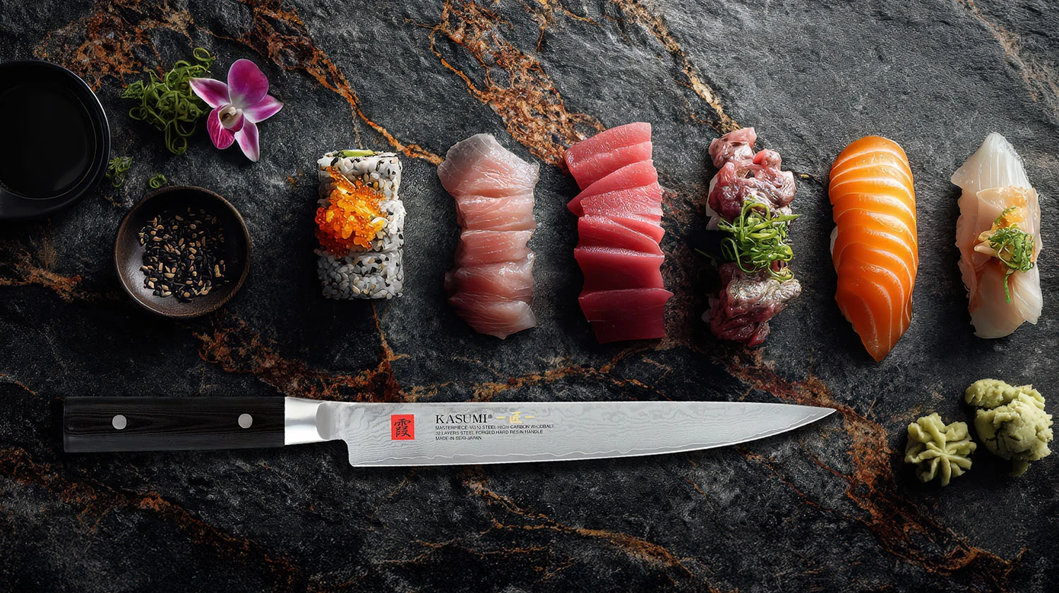 Japoński nóż Sujihiki z damasceńskiej stali VG-10, obok kawałków sushi i sashimi na kamiennej desce.