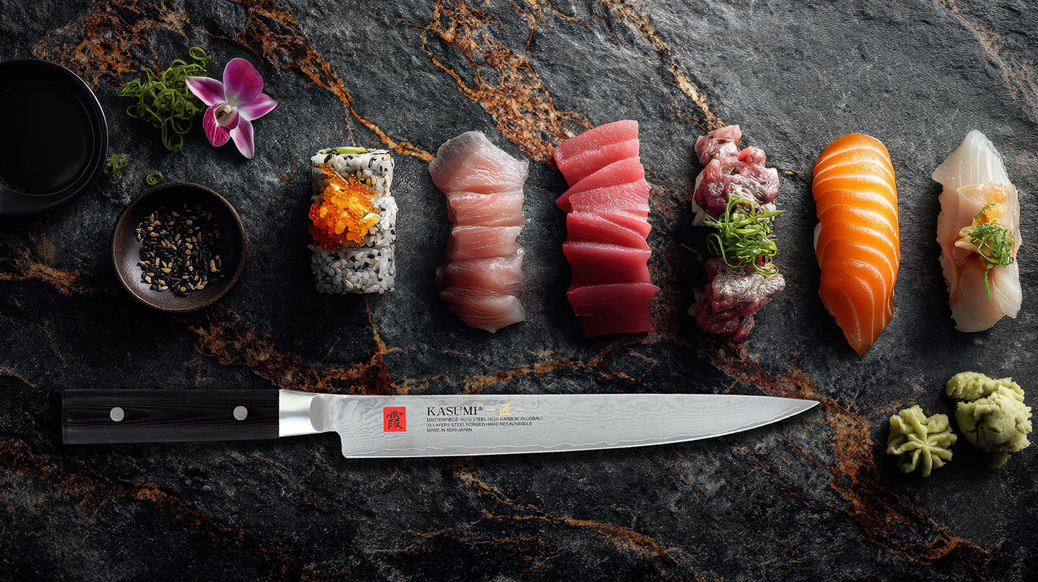 Japoński nóż Sujihiki z damasceńskiej stali VG-10, obok kawałków sushi i sashimi na kamiennej desce.