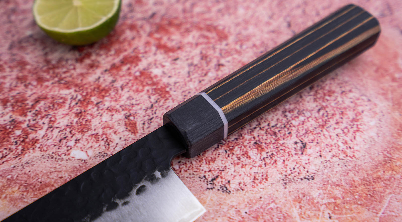 Japoński nóż Santoku z rękojeścią z ciemnego drewna na różowym tle.