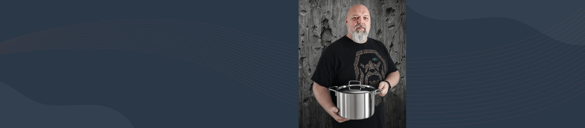 Mężczyzna prezentuje wysoki, stalowy garnek Demeyere 8L 5-Ply na tle betonowej ściany