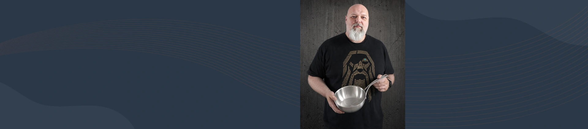 Mężczyzna prezentuje stalową patelnię sauté Atlantis 24 cm marki Demeyere na tle ciemnej ściany