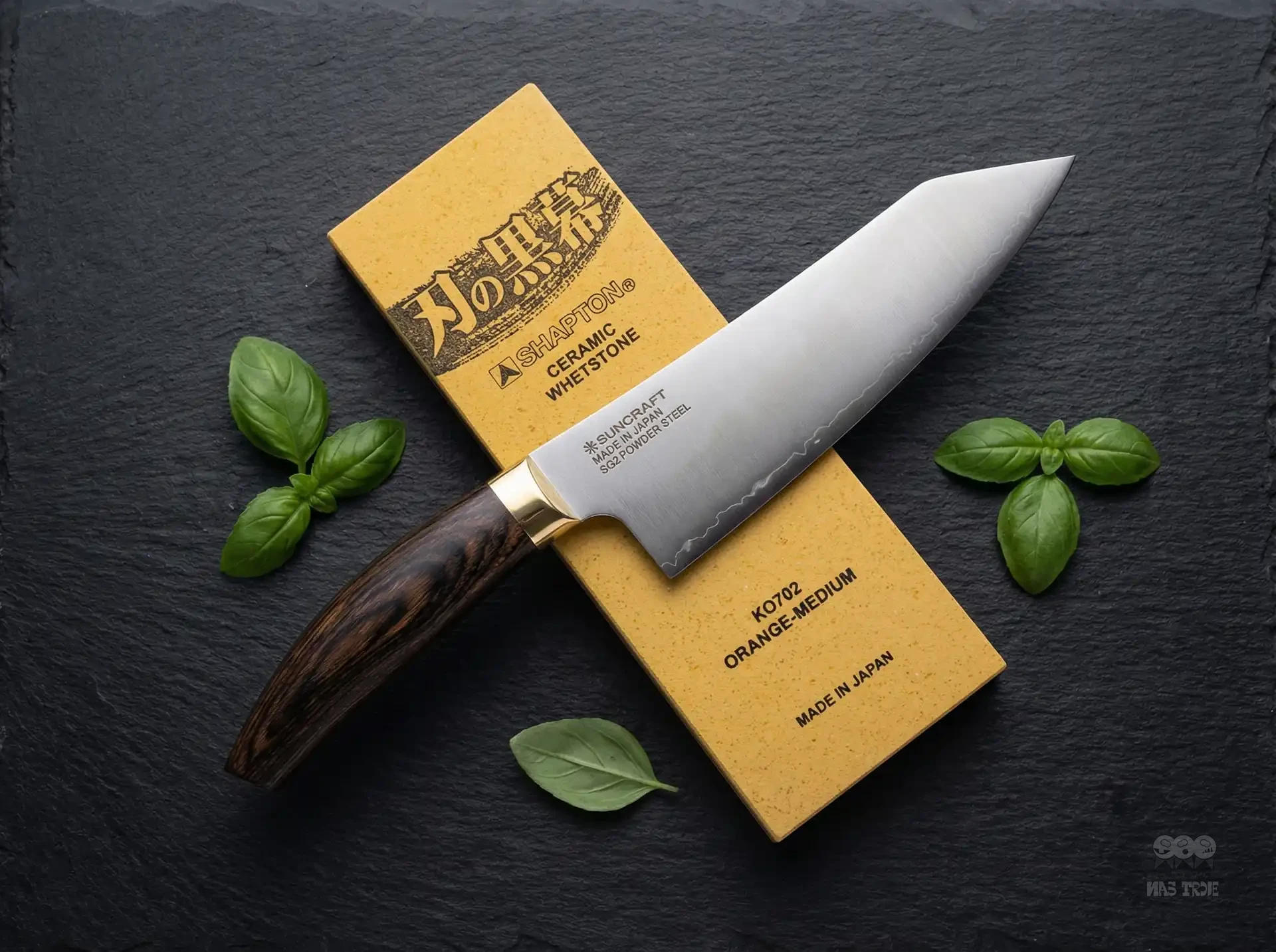 Japoński nóż Santoku Suncraft SG2 z elegancką rękojeścią, obok kamienia Shapton i liści bazylii na czarnym tle