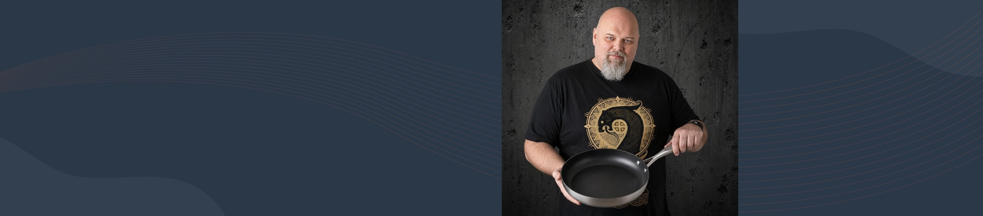 Mężczyzna prezentuje tytanowo-ceramiczną patelnię Scanpan o średnicy 26 cm na tle ciemnej ściany.