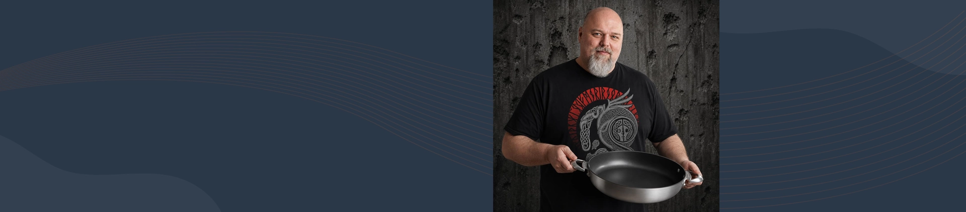 Mężczyzna prezentuje dużą patelnię tytanowo-ceramiczną Scanpan na tle ciemnej ściany.