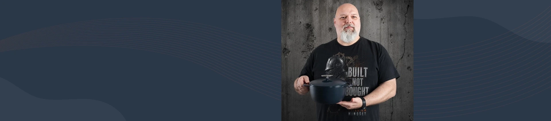 Mężczyzna prezentuje ciemnogranatowy, żeliwny garnek Indigo Unilloy 3,8 l na tle betonowej ściany.