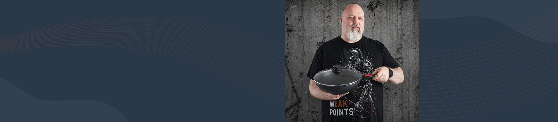 Mężczyzna prezentuje wok Diamond Lite z powłoką tytanową i odpinanym uchwytem na tle betonowej ściany
