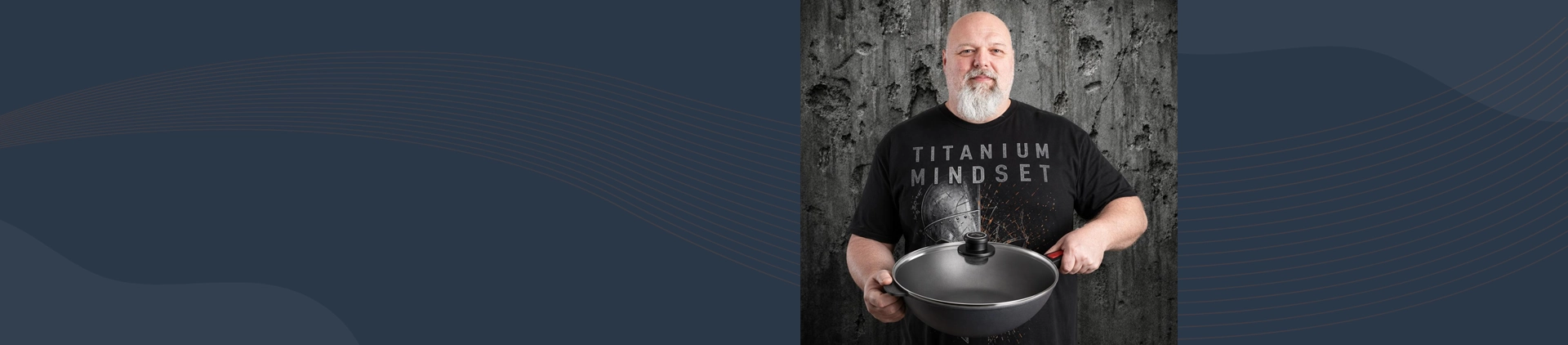 Mężczyzna prezentuje wok Diamond Lite z tytanową powłoką i odpinanym uchwytem na tle betonowej ściany