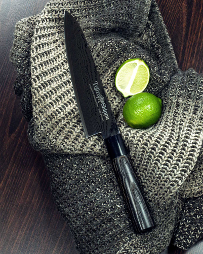 Czerniony nóż Tojiro Shippu Black Gyuto 24 cm na tle szarego materiału i limonek