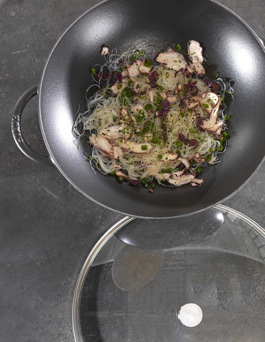 Żeliwny wok Staub Graphite Grey z potrawą z makaronem i warzywami na ciemnym tle.