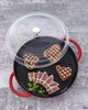 Szklana pokrywka Staub Universal Lid Ø 30 cm na czerwonej patelni z grillowanym mięsem.