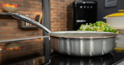 Patelnia sauté Falk Copper Core, stalowo-miedziana, na tle kuchni, Ø 18 cm.
