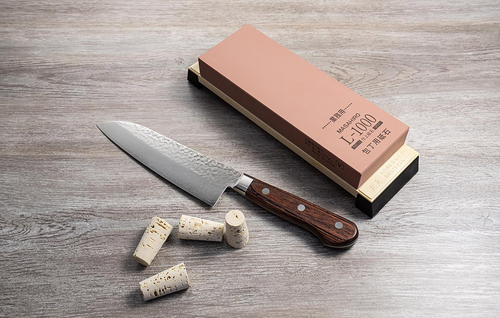 Nóż Santoku Senzo Universal Suncraft na drewnianym tle z korkami i ostrzałką