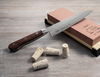 Senzo Universal Suncraft 33-warstwowy nóż Santoku na tle korków i kamienia.