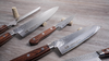 Japoński nóż Santoku Suncraft Senzo Universal z drewnianą rękojeścią na tle kuchennego blatu.