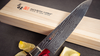 Nóż Santoku Mcusta Zanmai Ultimate Aranami z rdzeniem plecionej stali, 18 cm, na tle drewnianego pudełka.