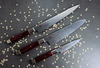 Mcusta Zanmai Ultimate Aranami - nóż Santoku 18 cm na tle dekoracyjnych elementów.
