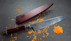Nóż Santoku Mcusta Zanmai Aranami, 18 cm, na tle czerwonej osłony i rozrzuconej soczewicy.