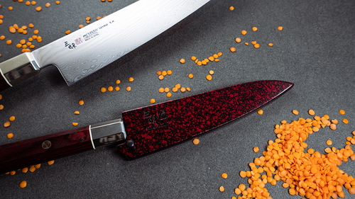 Nóż Santoku Mcusta Zanmai Ultimate Aranami na tle rozsypanej soczewicy.