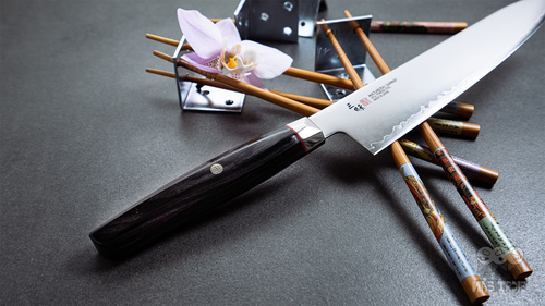 Japoński nóż Ko-Santoku Mcusta Zanmai Revolution na tle pałeczek i kwiatów.