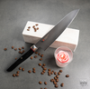 Japoński nóż Ko-Santoku Mcusta Zanmai Revolution na tle kawowych ziaren i świecy.