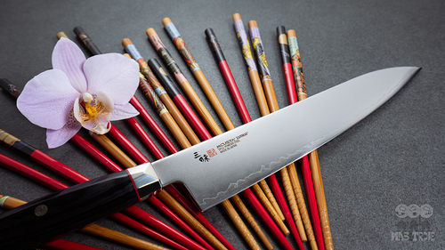 Nóż Santoku Mcusta Zanmai Revolution SPG2 na tle pałeczek i orchidei
