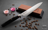 Japoński nóż Santoku Mcusta Zanmai Revolution, stal SPG2, 18 cm na tle ziaren kawy.