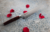 Nóż Santoku Mcusta Zanmai Revolution Red na dekoracyjnym tle z płatkami róż.