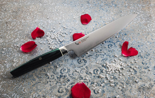 Nóż Kiritsuke Mcusta Zanmai Revolution na ozdobnym tle z płatkami róż.