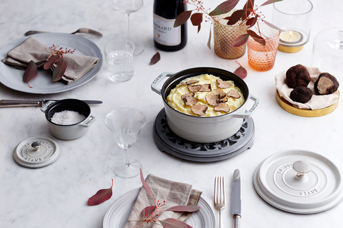 Owalny żeliwny garnek Staub White Truffle na elegancko nakrytym stole