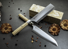 Nóż Santoku Mcusta Zanmai Beyond na kamiennym tle z suszonymi kwiatami.