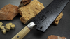Japoński nóż Santoku Mcusta Zanmai Beyond na tle kamieni