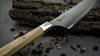 Nóż Santoku Mcusta Zanmai Beyond na rustykalnym tle z suszonymi owocami.