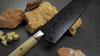 Japoński nóż Bunka Mcusta Zanmai Beyond, stal Aogami Super, 18 cm, na tle kamieni.