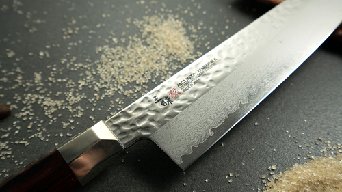 Nóż Sujihiki Mcusta Zanmai Supreme Hammered, damasceński, 24 cm, na tle rozsypanych przypraw.