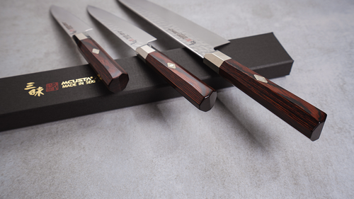 Mcusta Zanmai Santoku Supreme Hammered – nóż damasceński 18 cm na tle eleganckiego opakowania