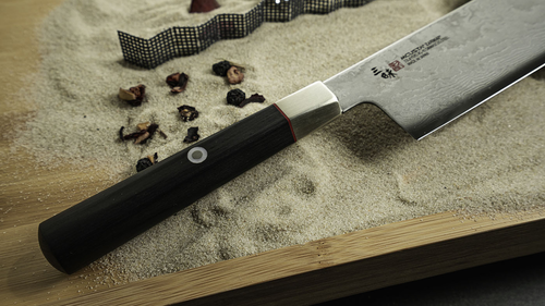 Japoński nóż Nakiri Mcusta Zanmai Splash Damascus na tle piasku.