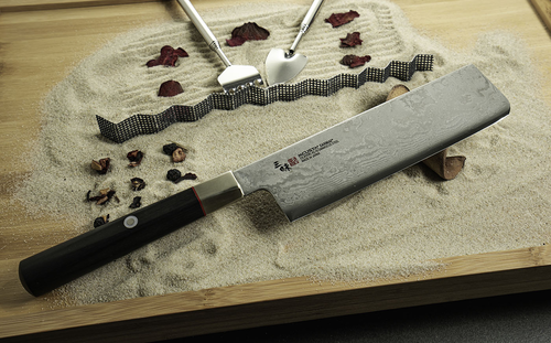 Japoński nóż Nakiri Mcusta Zanmai Splash Damascus na piaskowym tle.
