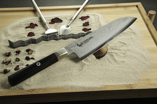 Nóż Santoku Mcusta Zanmai Splash Damascus na piaskowym tle z dekoracjami.