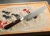 Nóż Santoku Mcusta Zanmai Supreme Ripple na piaskowym tle.
