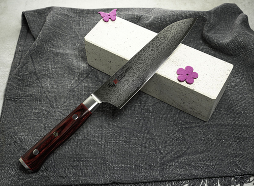 Nóż Gyuto Mcusta Zanmai Classic Pro Flame na tle kamienia z różową ozdobą.