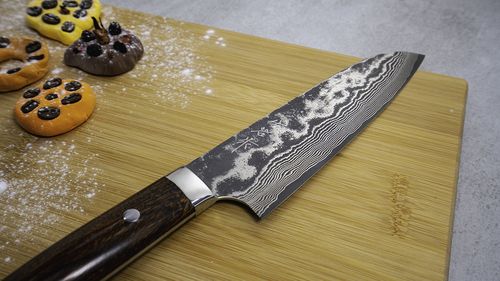 Ręcznie kuty nóż Santoku Takeshi Saji na desce z kolorowymi ciasteczkami