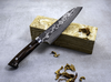 Ręcznie kuty nóż Santoku Takeshi Saji VG-10 na tle kamiennego bloku.