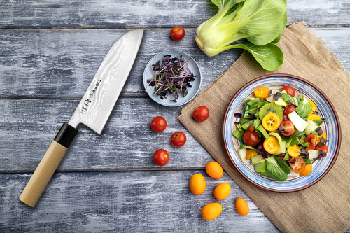 Japoński nóż Santoku Tojiro Shippu na drewnianym tle obok kolorowego talerza z sałatką.