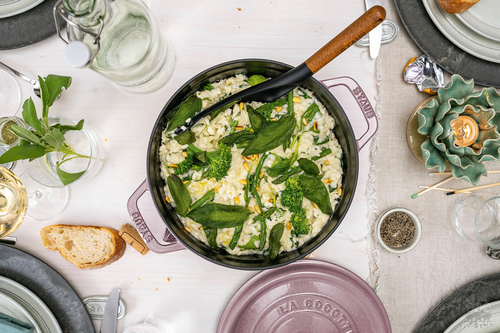 Żeliwny garnek Staub Sakura z risotto i warzywami, na elegancko nakrytym stole.