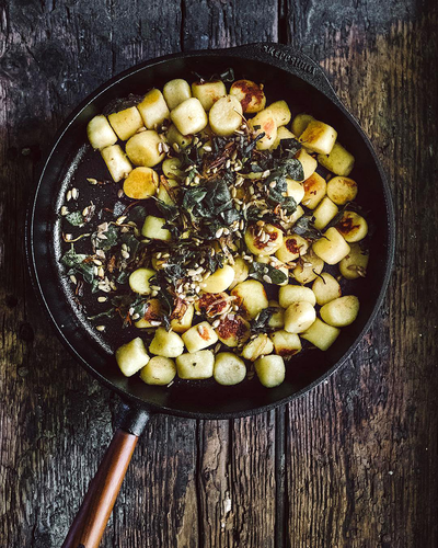 Żeliwna patelnia Skeppshult Walnut z uchwytem z orzecha, smażone gnocchi, rustykalne tło.