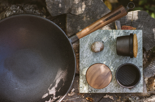 Wok Skeppshult Walnut z żeliwa, uchwyt z orzecha, na tle drewna i kamienia.
