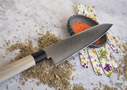 Gyuto Tojiro Shippu - japoński nóż kucharza 24 cm na tle przypraw i rękawicy.