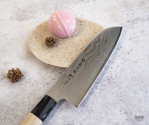 Japoński nóż Santoku Tojiro Shippu, 63-warstwowy, na tle kamiennej deski.